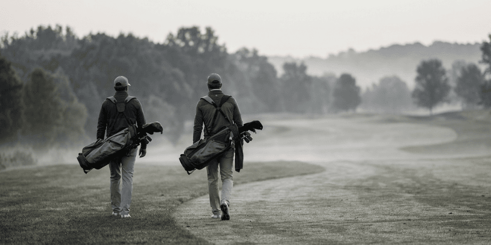 Two golfers walking on a misty fairway